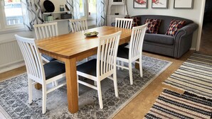 A dining area with a wooden table and white chairs, a grey sofa, and a patterned rug.