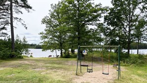 A park with a swing set, a sandy area, and a lake in the background.