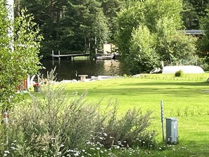 Une zone herbeuse avec une jetée qui s’avance dans un plan d’eau, entourée d’arbres et d’une structure blanche.