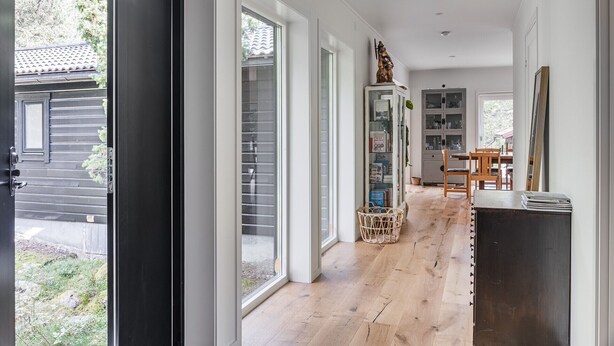 A spacious hallway with large windows, a wooden floor, and a dining area with a table and chairs.