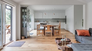 A spacious living area with a dining table and chairs, a grey sofa, and a kitchen in the background.