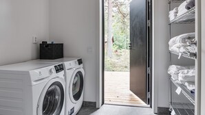 A laundry room with two front-loading washing machines, a black storage box, and a metal shelving unit with folded towels.