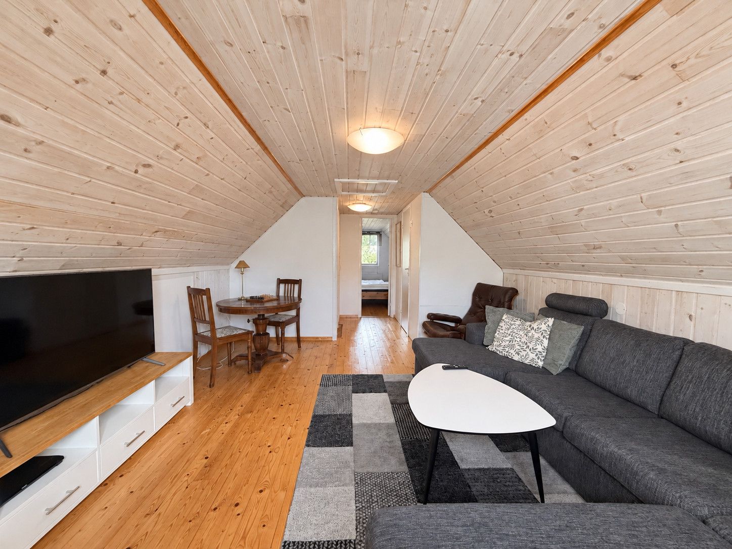 Une pièce confortable de style loft, avec un plafond en bois, un téléviseur à écran plat, un canapé, une table à manger avec des chaises et un escalier menant à un niveau supérieur.