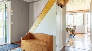 Un banco de madera en una habitación con techo inclinado, una zona de comedor con sillas y vistas a través de una ventana.