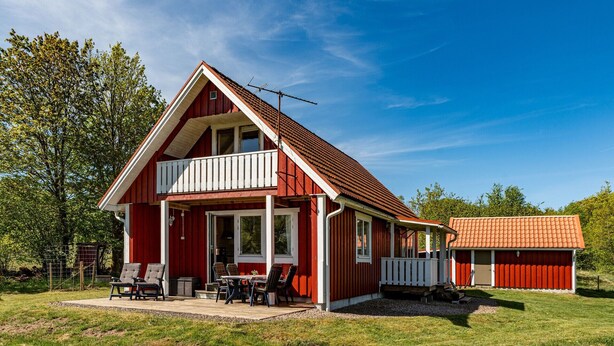 Una casa roja con balcón, un patio cercado y un edificio aparte con techo rojo.