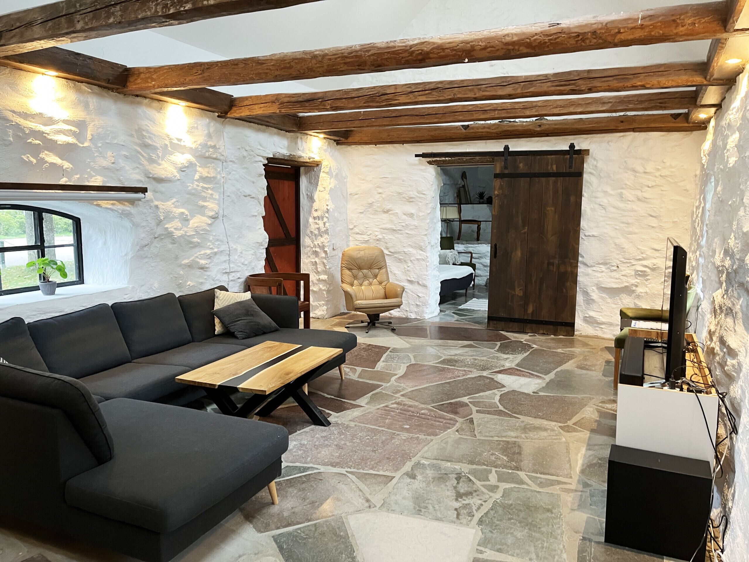 Une pièce avec un sol en pierre, un canapé, une chaise, une table en bois et un meuble pour la télévision.