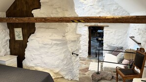 A room with a sloped ceiling, stone walls, a wooden beam, a bed, a chair, and a table.