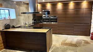 A modern kitchen with a central island, built-in ovens, and a stone-tiled floor.