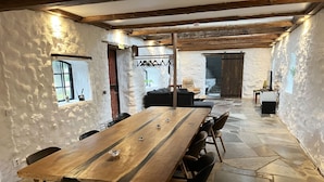 A rustic dining area with a long wooden table, black chairs, stone flooring, and exposed wooden beams.