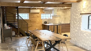 A rustic interior with a wooden dining table, stone flooring, and exposed wooden beams.