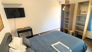Une chambre à coucher comprenant un lit, un téléviseur fixé au mur, une table de chevet et une armoire.