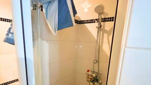 Une douche avec une porte en verre, un pommeau de douche amovible et une petite étagère pour les articles de toilette.