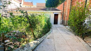 Un étroit sentier pavé mène à un bâtiment dont le toit est recouvert de tuiles rouges.