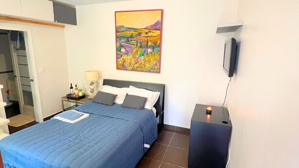 Une chambre à coucher avec un lit, une table de chevet avec une lampe, un tableau accroché au mur et un téléviseur fixé au mur.