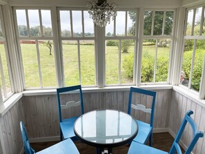 A conservatory with a round glass table and blue chairs, large windows with a view of a grassy field.