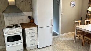 Una cocina compacta con estufa, horno y refrigerador, una mesa de comedor con sillas, y un reloj en la pared.