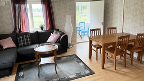 Una sala de estar con sofá, mesa de centro, mesa de comedor con sillas y vista a un espacio exterior a través de una puerta.