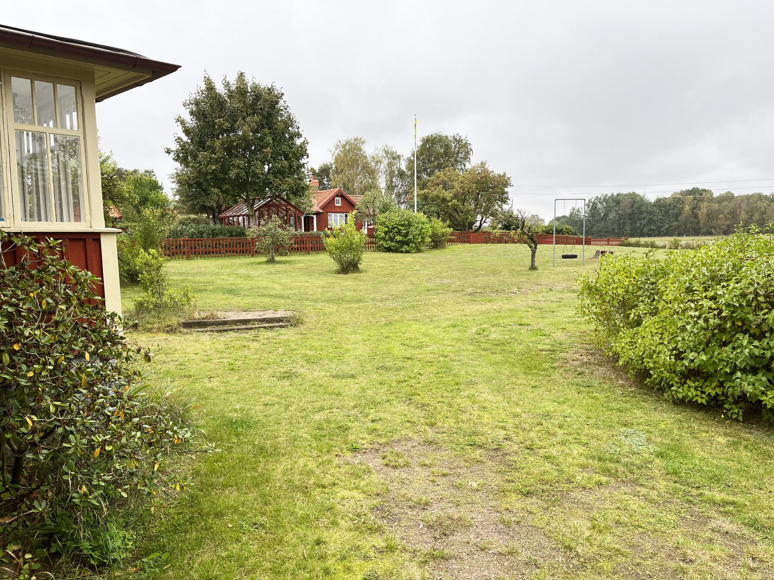 A residential property with a well-maintained lawn, a wooden fence, and a red-roofed house.