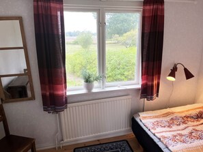 A bedroom with a window, a radiator, a bedside lamp, and a bed with a patterned blanket. - Nice cottage located close to a bay in Skäppevik I SE05046 (Bergkvara)