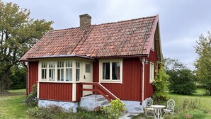 Una casa de madera roja con techo de tejas, un pequeño porche y una silla blanca en el exterior.