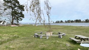 Un espacio con césped, un pozo de fuego circular de piedra, mesas de picnic y una mesa redonda pequeña.