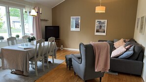 Un soggiorno con un divano grigio, un tavolo da pranzo con sedie, una TV e opere d'arte alle pareti.