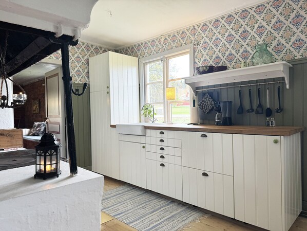 A kitchen with white cabinets, a window, and a hanging rack with kitchen utensils.