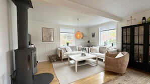 Un salón acogedor con chimenea, sofás blancos, una mesa de centro y una butaca de mimbre.