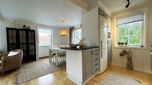 Una cocina moderna con armarios blancos, un comedor con mesa y sillas, un mueble negro y una ventana con plantas.