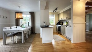 Una cocina moderna con armarios blancos, un comedor con una mesa y sillas blancas, y un ventanal grande.