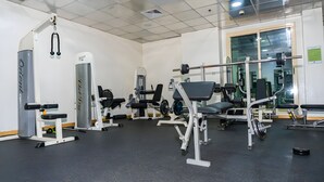 Uma academia com diversos equipamentos de exercícios, incluindo máquinas de peso e pesos livres, dispostos em um espaço amplo com piso cerâmico e grandes janelas.