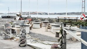 Zona ribereña con asientos de hormigón, barandilla metálica y vista al mar.