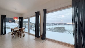 A spacious room with a large sliding glass door leading to a snowy outdoor area, a dining table with chairs, and a hanging light fixture.