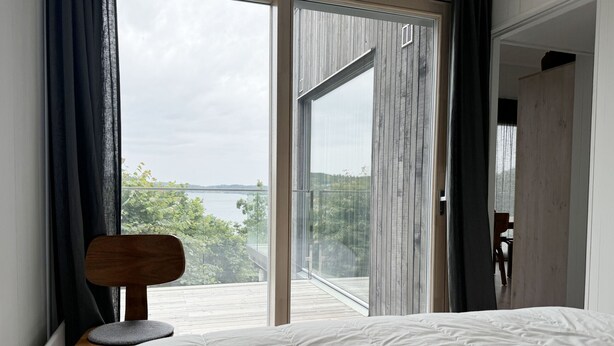 A bedroom with a large bed, a chair, a view of a lake, and a sliding door leading to a balcony.