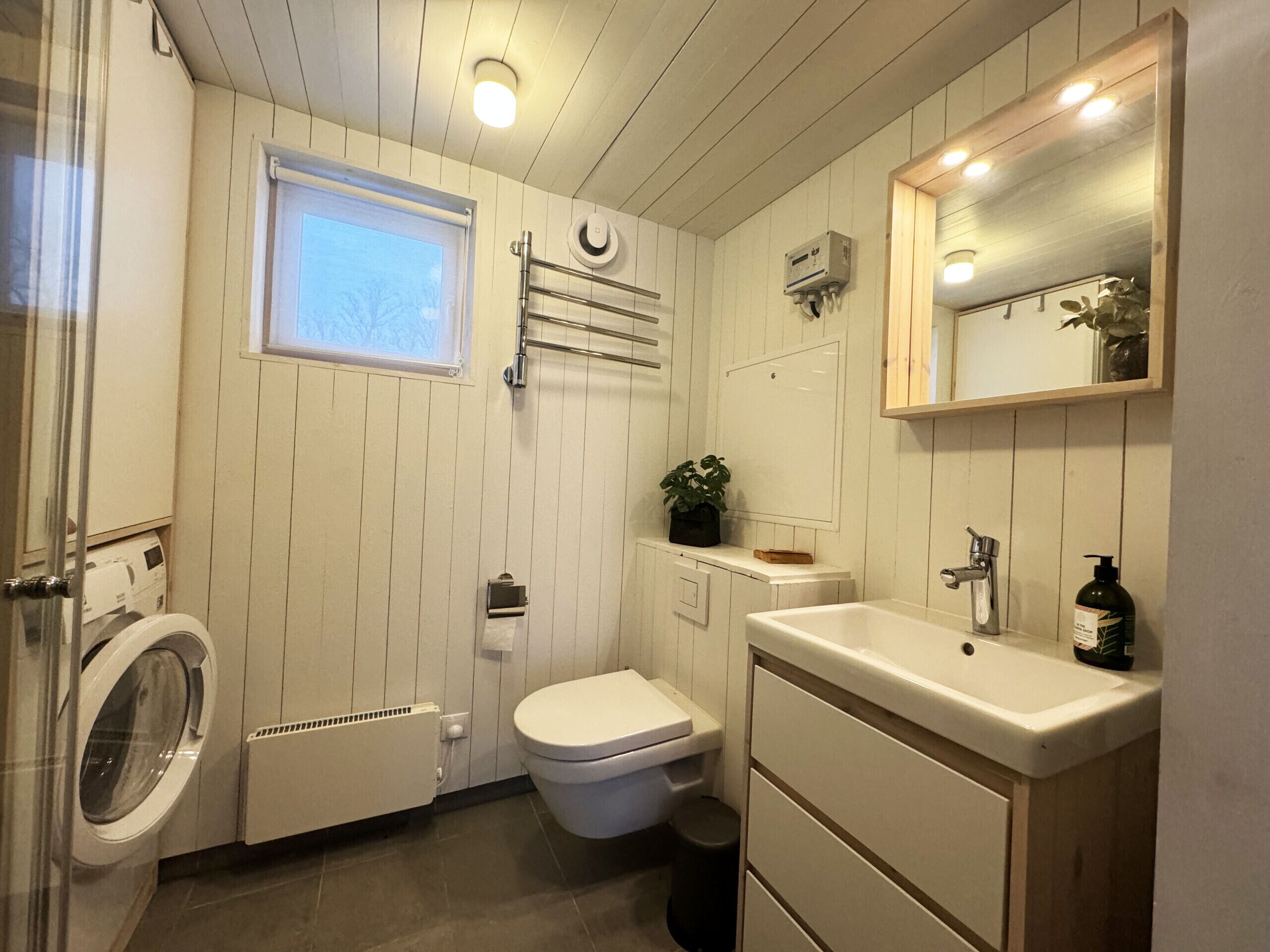 Ein kleines Badezimmer mit Waschmaschine, Toilette, Waschbecken und einem kleinen Fenster.