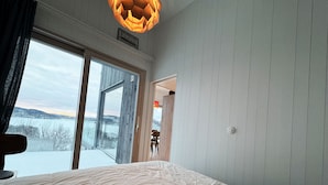 A bedroom with a large bed, a view of a snowy landscape through a sliding door, and a wooden ceiling light fixture.