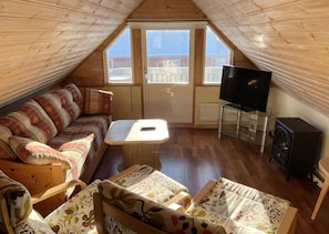 Een gezellig zolderkamer met een houten schuine dak, een bank, een kleine tafel, een televisie en een open haard.