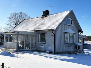 Een huis met twee verdiepingen, een metalen dak, een veranda met een bankje en een zichtbare schoorsteen.