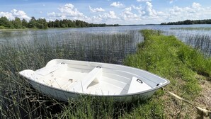 A small boat tied to a grassy bank by a calm lake with a forest in the background.