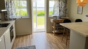 A kitchen with a wooden countertop, a dining area with a table and chairs, and a view of a lake through the open door.