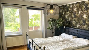 A bedroom with a bed, a window, a radiator, a plant, and a wall with a leafy pattern. - Large and spacious villa located in Storebro close to a nice swimming area | SE05059 (Storebro)