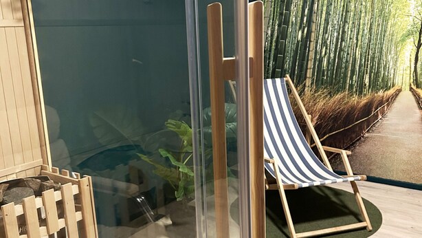 A room with a glass wall, a wooden chair, and a bamboo forest view. - Large and spacious villa located in Storebro close to a nice swimming area | SE05059 (Storebro)