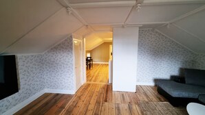 Ein Schlafzimmer im Dachgeschoss mit Holzdielen, einem grauen Sofa und einer Wand mit Muster.