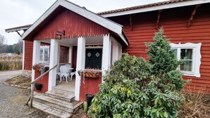 Ein rotes Holzhaus mit Veranda, weißen Stühlen und Topfpflanzen.