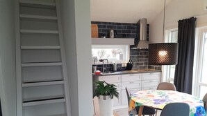 Une cuisine moderne avec un dosseret de carreaux noirs, une hotte de cuisine en acier inoxydable et un coin repas avec une table dressée pour deux personnes.
