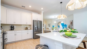 A modern kitchen with white cabinets, stainless steel appliances, and a central island with a green bowl.
