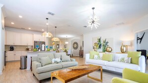 A spacious living room with a sofa, coffee table, and a dining area with a chandelier.