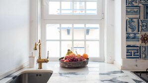 Une cuisine dotée d’un plan de travail en marbre, d’un évier, d’une fenêtre offrant une belle vue et d’un saladier rempli de fruits.