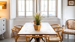 Une table à manger agrémentée d’une plante en pot, entourée de chaises en bois, dans une pièce dotée d’une grande fenêtre et d’un luminaire suspendu.