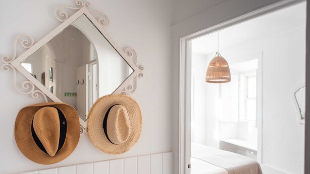 Une pièce avec un lit, un miroir et deux chapeaux accrochés au mur.